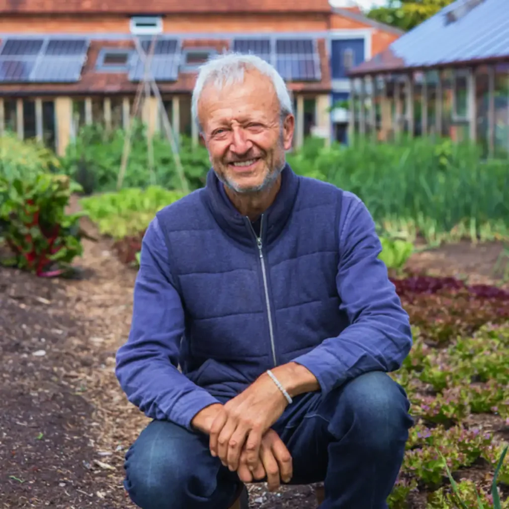 Person kneeling in vegetable garden, solar panels behind.